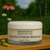 Éminence Organic Skin Care Clear Skin Probiotic Moisturizer potje, op een houten ondergrond met een bloemrijke achtergrond.