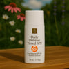 Éminence Organic Skin Care Daily Defense Tinted SPF flesje, op een houten ondergrond met een bloemrijke achtergrond.
