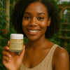 Een persoon die het Éminence Organic Skin Care Turmeric Energizing Treatment potje vasthoudt, in een natuurlijke buitenomgeving met groen op de achtergrond.